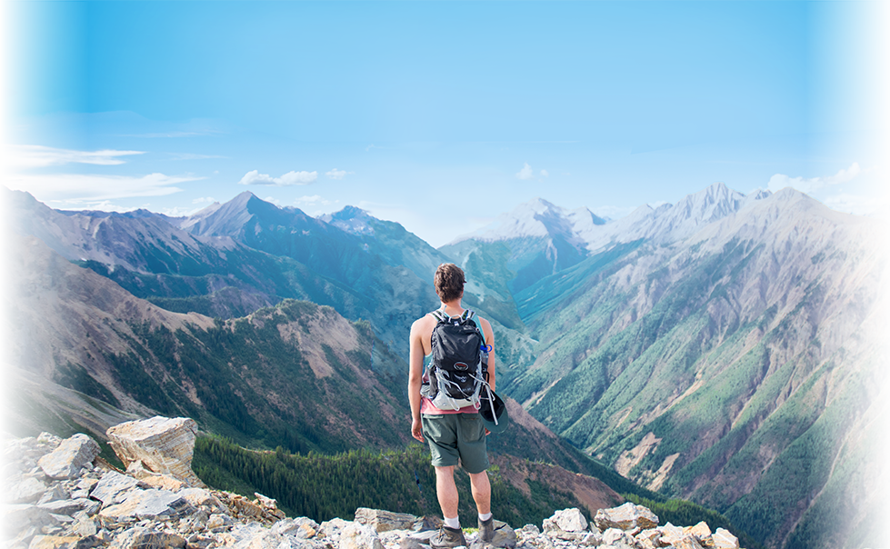 男性が山の頂上に上り、そこから景色を眺めている様子を背中から写した写真